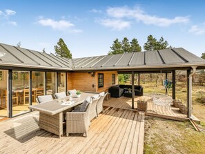 Une maison moderne dotée d’un patio couvert, de mobilier d’extérieur et offrant une vue sur le paysage environnant.