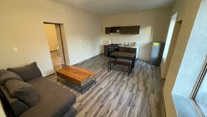 Un salon moderne avec un canapé, une table basse en bois et un coin cuisine équipé d’une cuisinière et d’un évier.