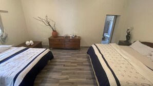 Une chambre avec deux lits, une commode, un vase avec des branches et un miroir au mur.