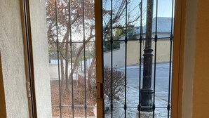 Une porte-fenêtre coulissante avec des barreaux métalliques, un pot de fleurs sur la gauche et une zone dallée de pierres à l’extérieur.