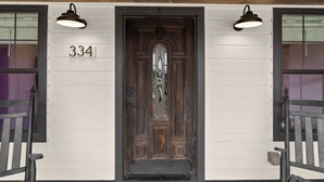 Uma porta de madeira com o número '334' em cima, duas luzes fixadas na parede e um banco à esquerda.