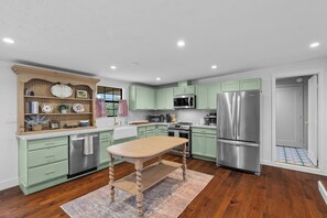 A kitchen with green cabinets, stainless steel appliances, a wooden table, and a patterned rug. - Spacious 4-bedroom home in beautiful Fredericksburg (Fredericksburg)