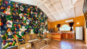 A room with a large abstract mural, wicker furniture, a kitchen area, and a tiled floor. - Painted house- 4 pax, 4 min from the beach (Las Galeras)