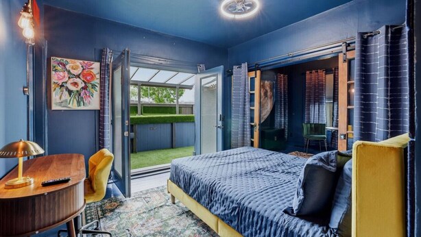 Un dormitorio con cama, escritorio, silla, ventana y puerta que da a un balcón.