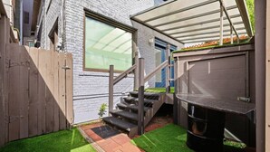 Un patio trasero con una escalera de madera, una parrilla para barbacoa y un área de patio techada.