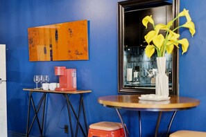 A room with a blue wall, a coffee machine, a vase with yellow flowers, and a framed picture. - Retro 1 Bd Apt near Montrose! (Houston)