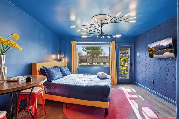 Un dormitorio moderno con cama, escritorio, silla, ventana y televisor instalado en la pared.