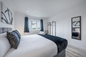Une chambre à coucher moderne, dotée d’un grand lit, offrant une vue sur l’extérieur par une fenêtre, et d’un porte-manteau en métal noir.
