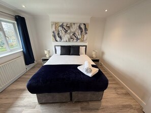 Une chambre moderne avec un grand lit, une tête de lit ornée d’une œuvre d’art abstraite, une fenêtre avec des rideaux et un radiateur.