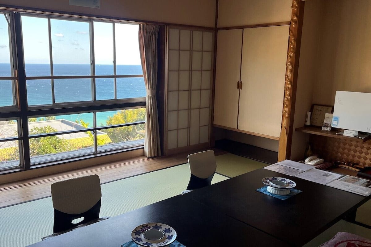 Een kamer met tatami matten, een tafel met een laptop, en uitzicht op de oceaan.