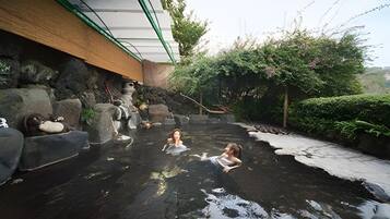 Een warmwaterbrongebied met stenen traptreden die het water in leiden, omringd door groen en een gebouw met een groen dak.