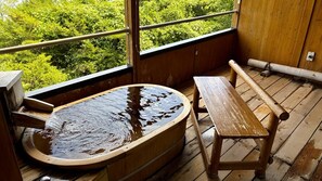 Een houten jacuzzi met een bank, een houten tafel en uitzicht op weelderige begroeiing door grote ramen.