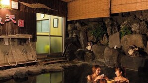 Un onsen japonais traditionnel, avec un intérieur en bois, un bain en pierre et une vue sur un bâtiment traditionnel.