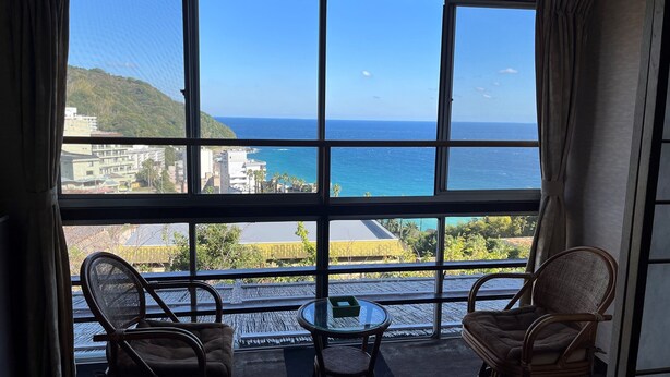 Un balcon avec vue sur la mer, deux fauteuils en osier et une petite table.