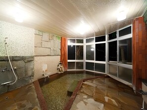 Een kamer met een stenen muur, een klein beeldje en een raam met veel ruiten.