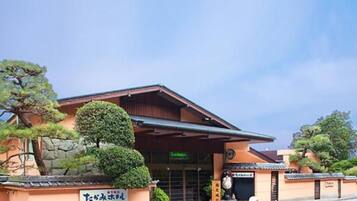 A traditional Japanese building with a covered entrance, signage, and well-maintained landscaping.