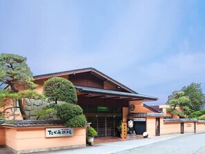 A traditional Japanese building with a covered entrance, signage, and well-maintained landscaping. - Takami Hotel (Higashiizu)