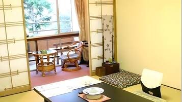 A traditional Japanese room with tatami flooring, a low table with a plate and chopsticks, and a sliding door leading to a balcony with a view of trees.
