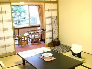 A traditional Japanese room with tatami flooring, a low table with a plate and chopsticks, and a sliding door leading to a balcony with a view of trees. - Takami Hotel (Higashiizu)