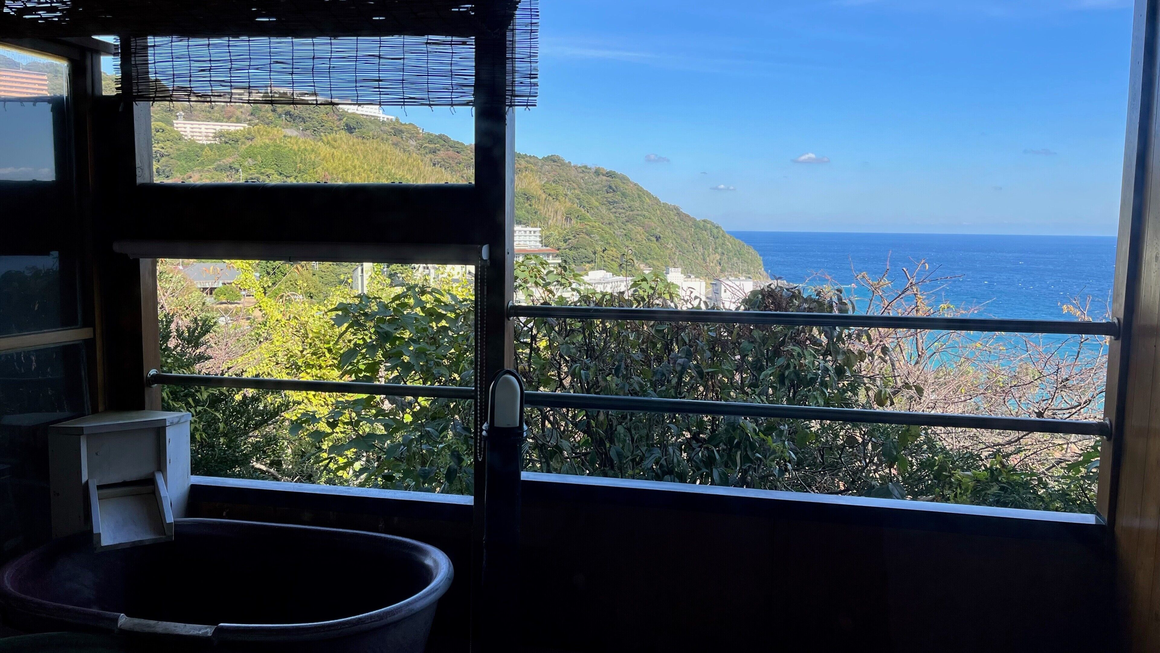 Ein Zimmer mit Meer- und Hügelblick, ein Fenster mit Jalousien und ein Mülleimer.