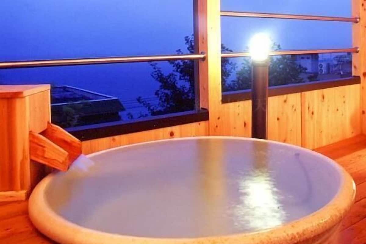 Een houten interieur met een groot ovaalvormig bubbelbad en een raam met uitzicht op een gebouw.