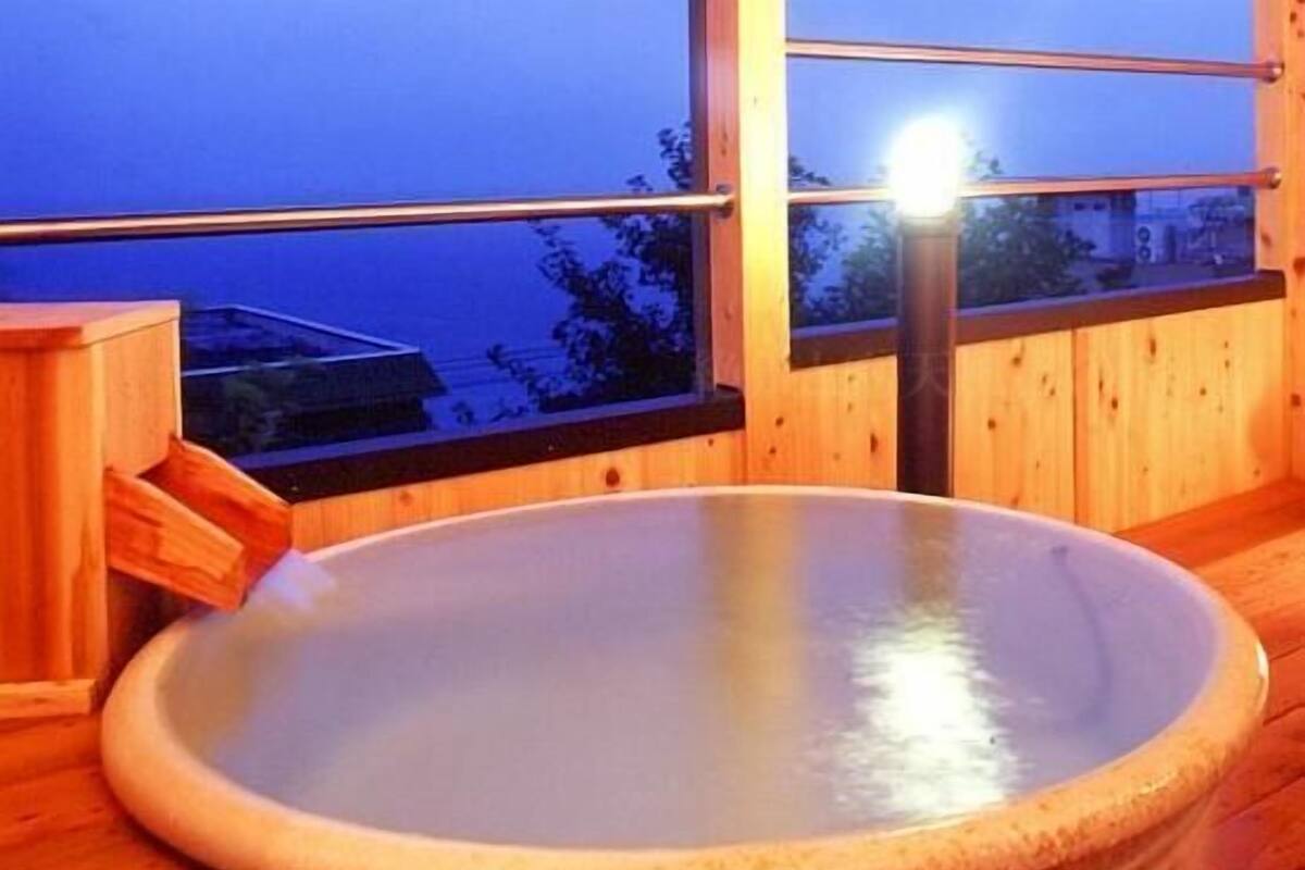 Ein Holzinnenraum mit einer großen, ovalen Whirlwanne und einem Fenster mit Blick auf ein Gebäude.