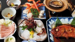 Diverse gerechten, waaronder zeevruchten, sashimi en een hele vis, gepresenteerd op een tafel met meerdere kleine schalen en kommetjes.