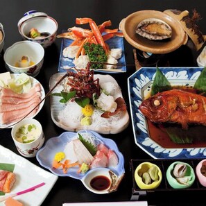 Verschiedene Gerichte, darunter Meeresfrüchte, Sashimi und ein ganzer Fisch, angerichtet auf einem Tisch mit mehreren kleinen Schälchen und Tellern.