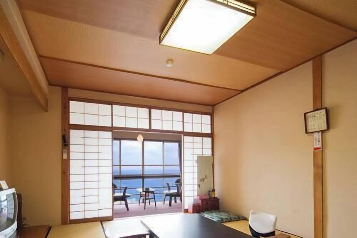 Een traditionele Japanse kamer met tatami vloerbedekking, een lage tafel, een bank en uitzicht op zee.