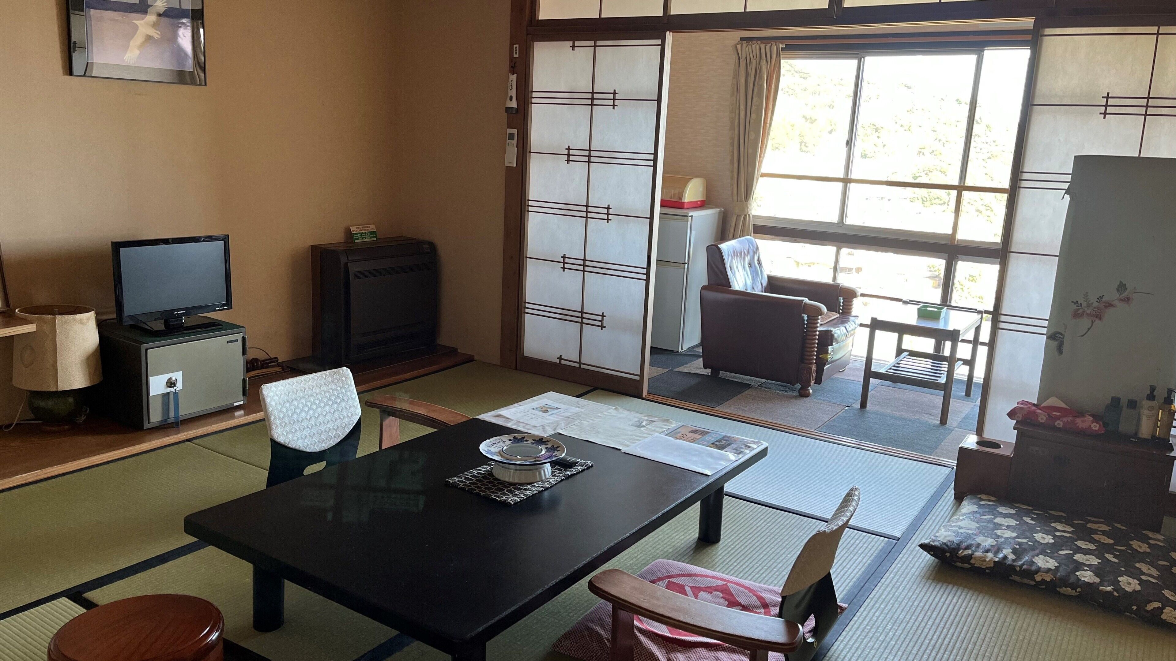 Ein traditioneller japanischer Raum mit Tatami-Böden, einem niedrigen Tisch, einem Fernseher und einer Schiebetür zu einem Außenbereich.