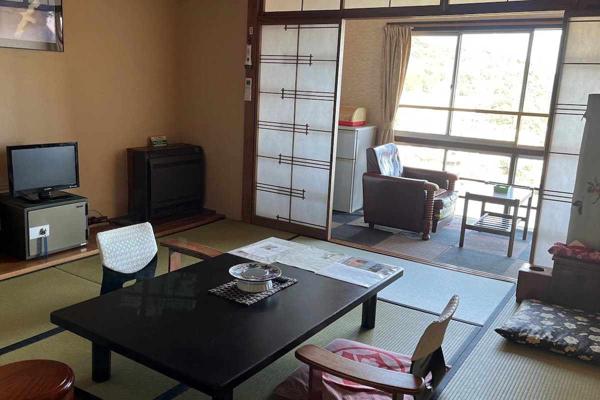 Een traditionele Japanse kamer met tatami vloerbedekking, een lage tafel, een televisie en een schuifdeur naar een buitenruimte.