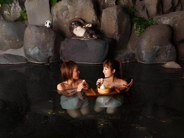 Two individuals in a stone-walled area with a reflective surface, possibly a pool, and a small boat.