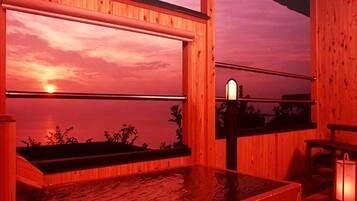 A wooden spa bath with a view of the sunset over water.