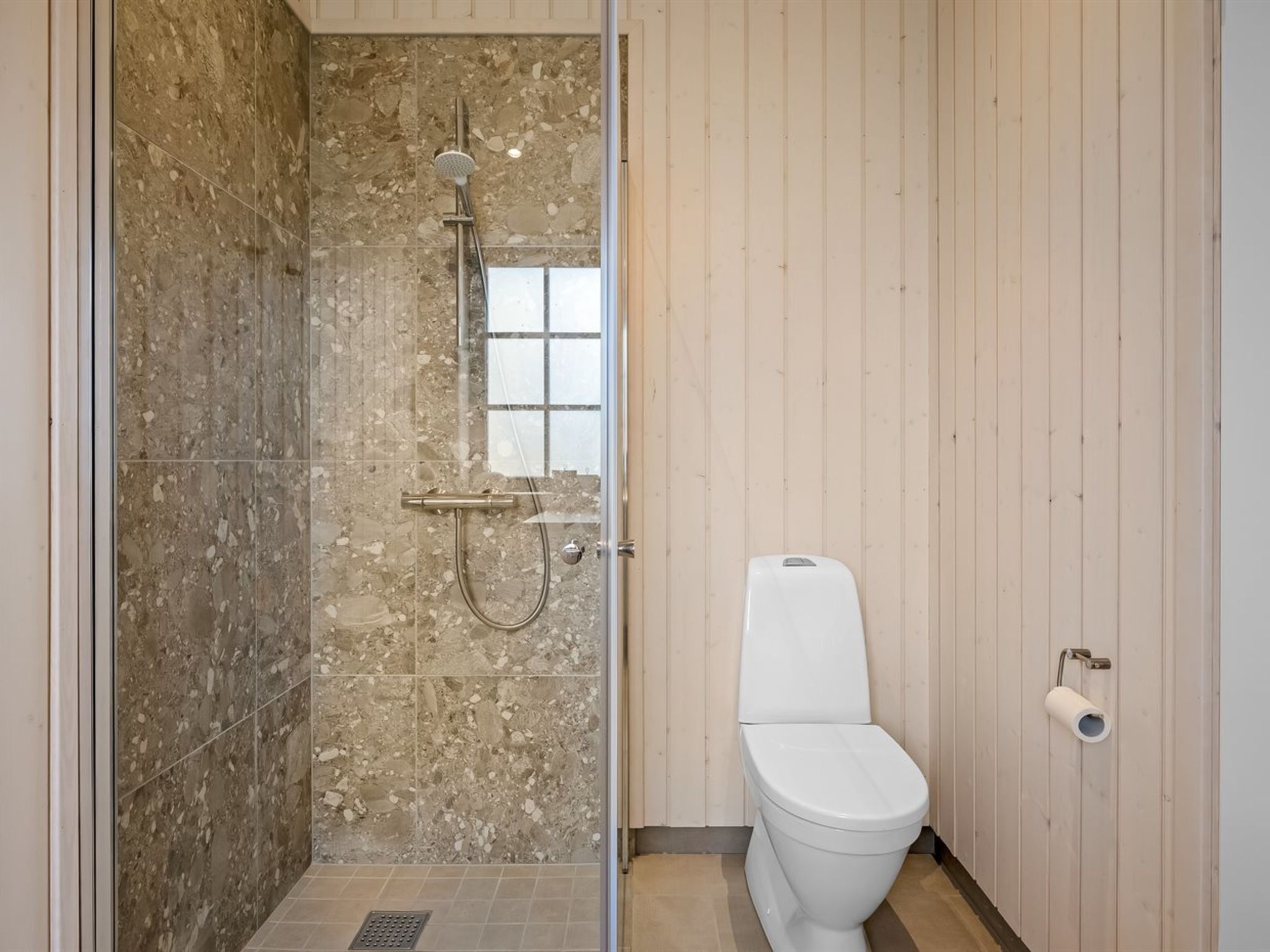 Een badkamer met een douche, toilet en een houten wand.