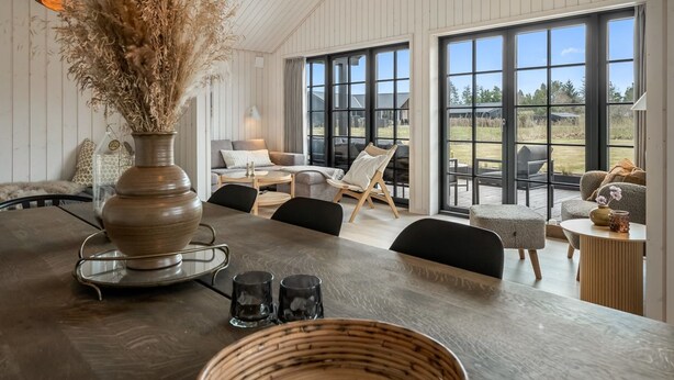 A spacious room with a large dining table, a sofa, and a chair, with a view of the outdoors through large windows. - "Emin" - 2.8km from the sea by Interhome (Henne)