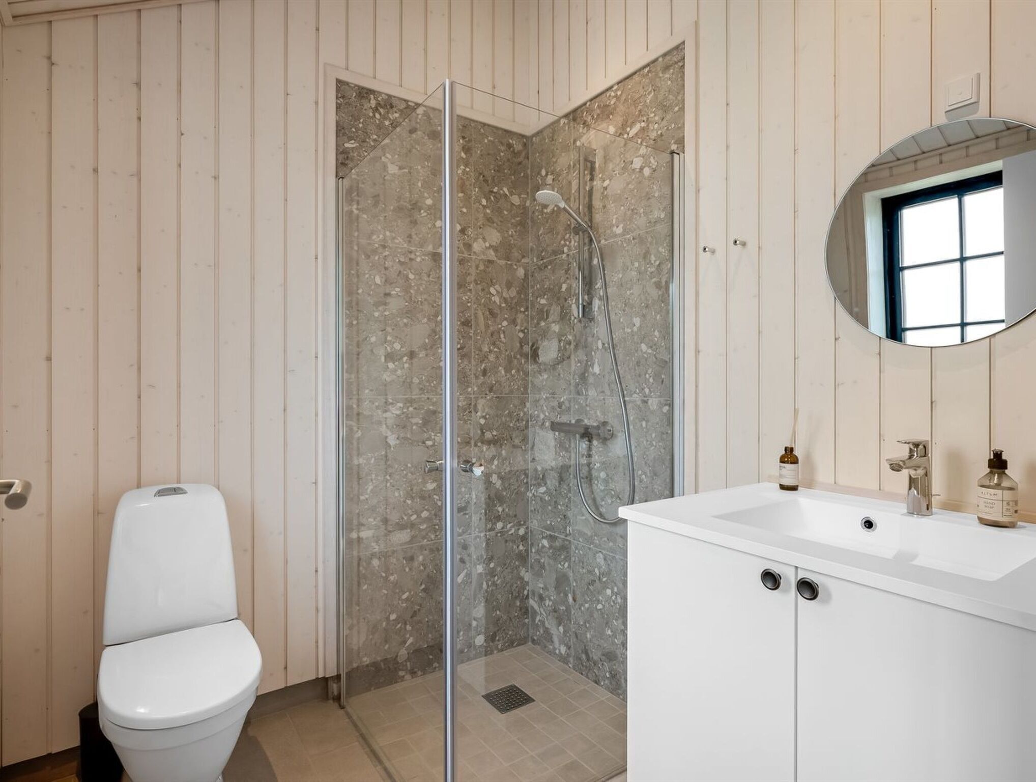A bathroom with a glass-enclosed shower, a white toilet, and a white vanity with a mirror.
