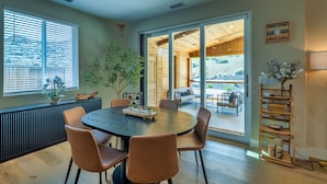 Un coin repas avec une table ronde, quatre chaises, une plante en pot et une vue sur une terrasse extérieure, visible à travers des portes vitrées.