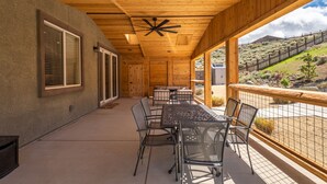 Une terrasse couverte avec une table et des chaises, un plafond en bois et une vue sur un paysage vallonné.
