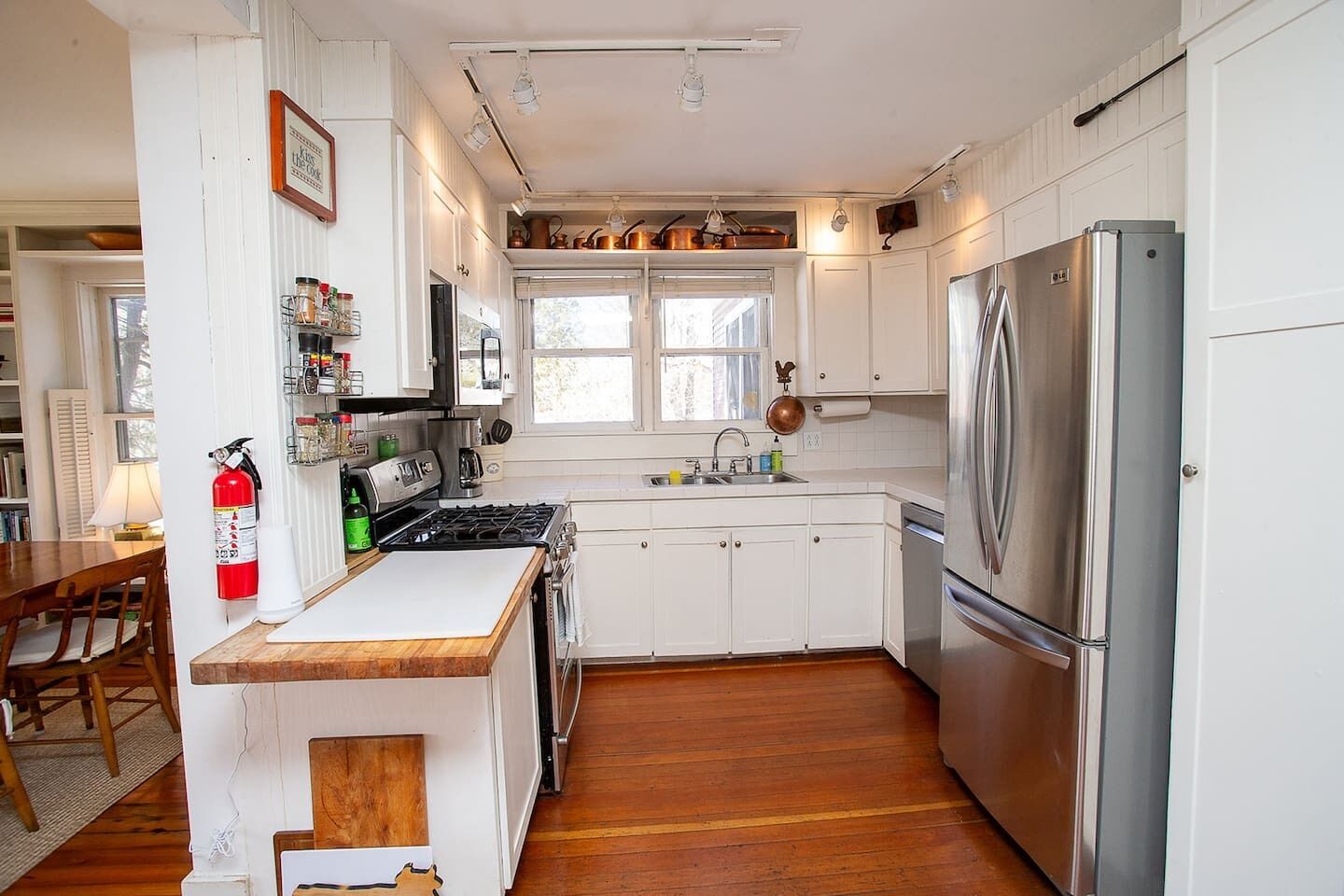 A kitchen with white cabinets, stainless steel appliances, a wooden countertop, and a window above the sink.