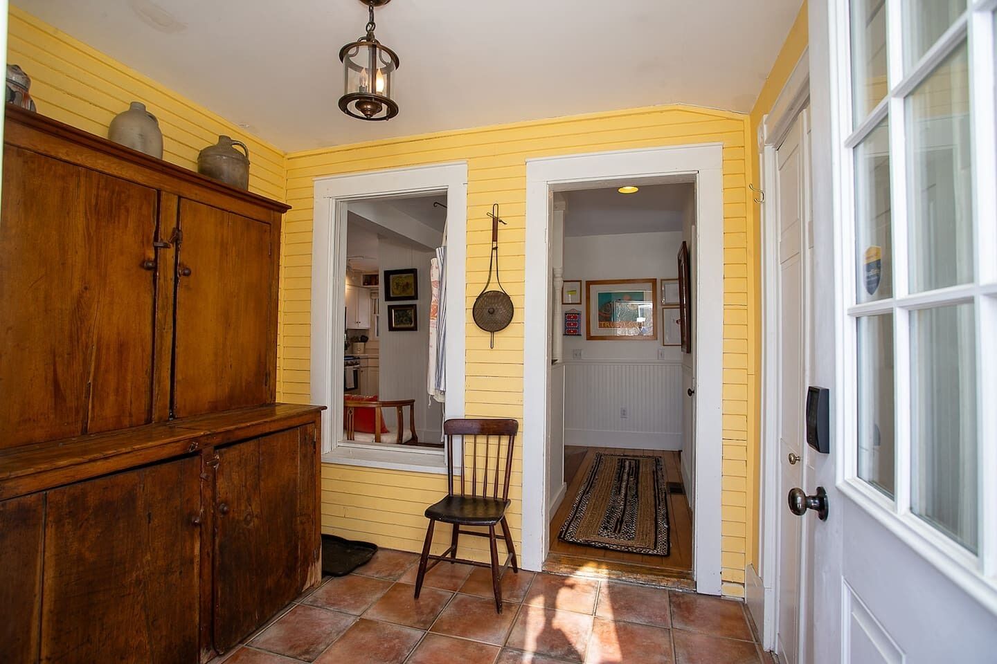 A yellow-walled interior with a wooden cabinet, a chair, and a door leading to another room.