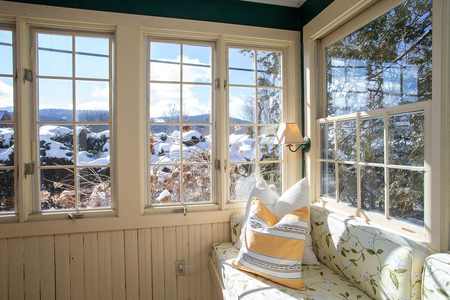 Una habitación con un muro revestido de madera, un asiento junto a la ventana con cojín y vistas a un paisaje nevado.