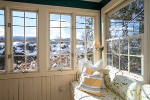 Ein Zimmer mit einer holzverkleideten Wand, einer Sitzbank mit Kissen und Blick auf eine verschneite Landschaft.