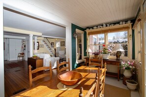Un comedor acogedor con una mesa de madera, sillas y un tazón grande. Una escalera conduce a otra habitación, y una ventana ofrece vistas al exterior.