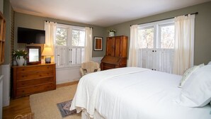 A bedroom with a bed, dresser, television, and windows with shutters.