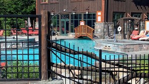 Un espace piscine entouré d’une clôture en bois, avec des chaises longues et, au fond, un bâtiment doté de grandes fenêtres.
