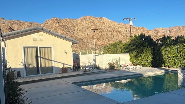 Un giardino con piscina, patio con sedie e montagne sullo sfondo.