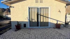 Una casa con un patio piastrellato, una porta scorrevole in vetro e due piante in vaso.