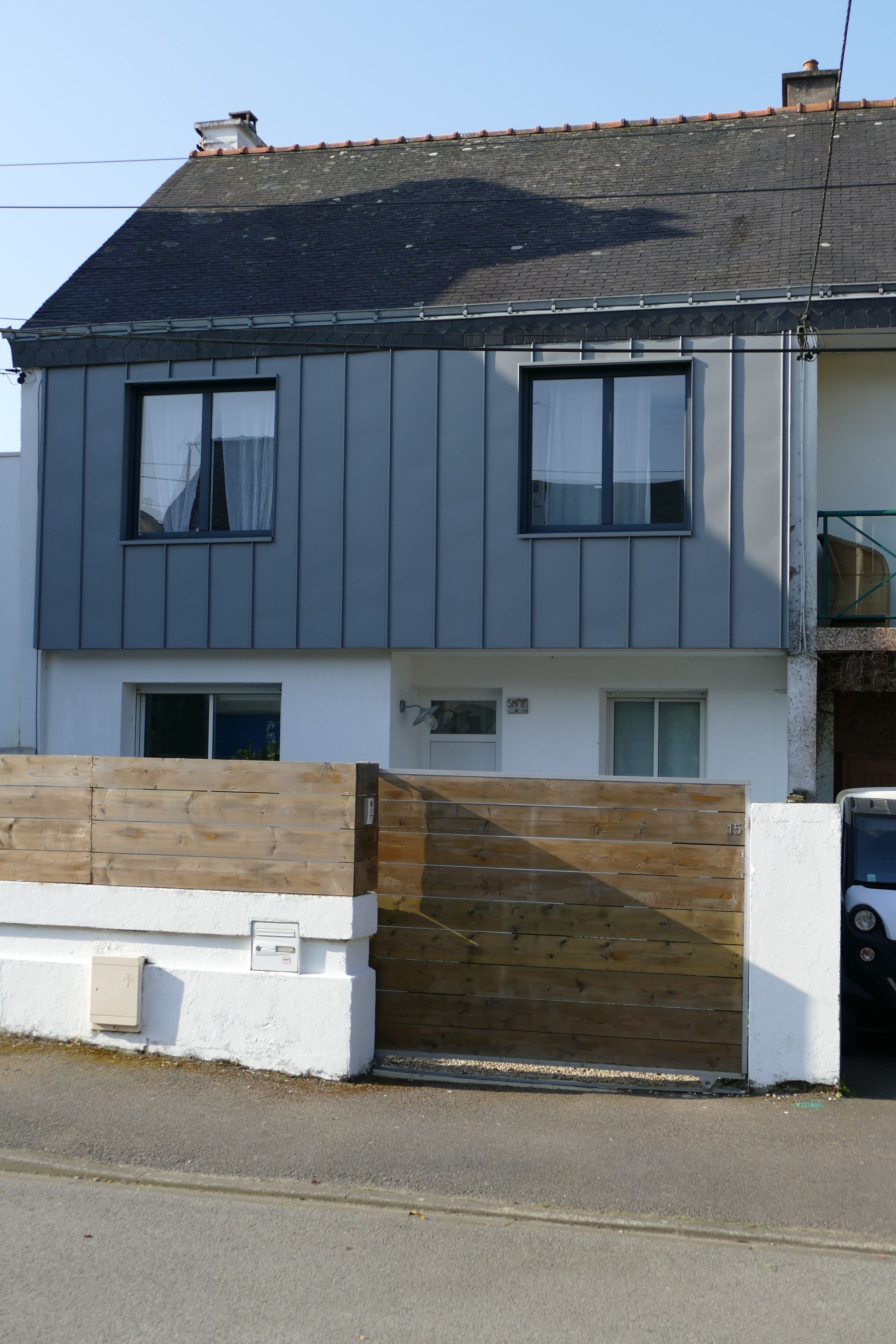 Un immeuble résidentiel de deux étages, doté d’une façade grise, d’un portail en bois et d’une porte de garage visible.