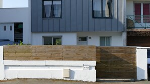 Ein zweigeschossiges Wohnhaus mit Holzzaun, befestigtem Eingangstor und einem kleinen Technikschacht.