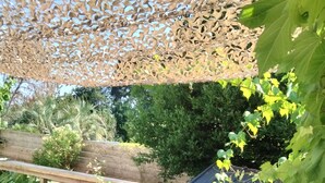 Eine Terrasse im Freien mit einem Holztisch und -stühlen, umgeben von Grünpflanzen und einem dekorativen Gitter.